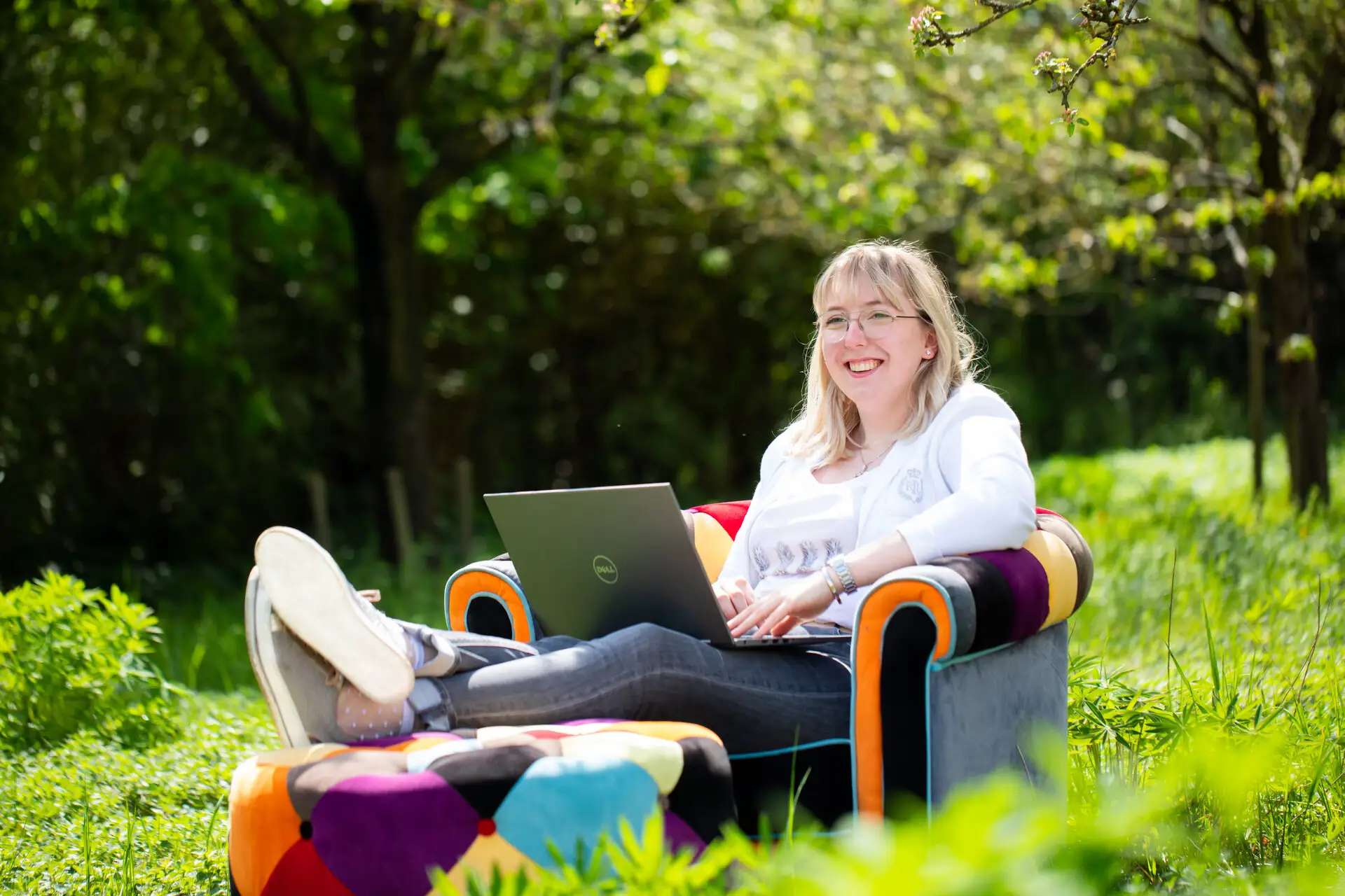 Victoria Reker, Teil des Gebäudereinigungsunternehmen in fünfter Generation, sitzt im Grünen auf einem bunten Sessel, den Laptop auf ihrem Schoß.